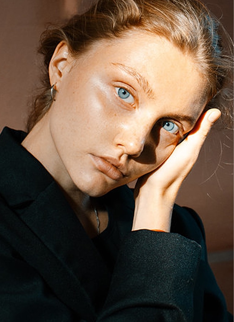 Woman with blue eyes resting her hand on face.