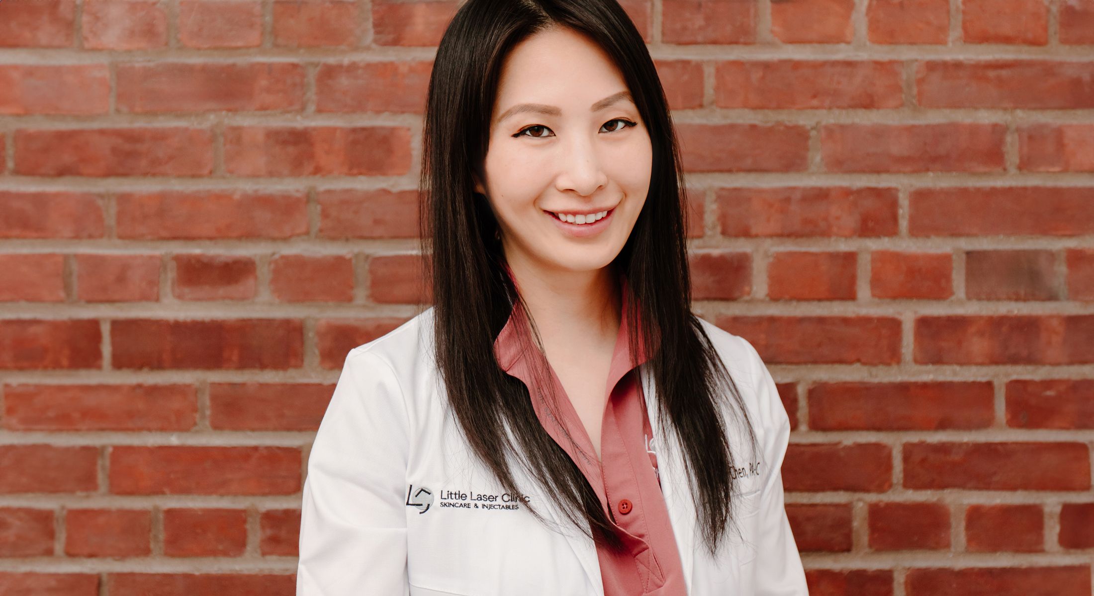 Little Laser Clinic founder, Christine Chen, in white coat against brick wall background.
