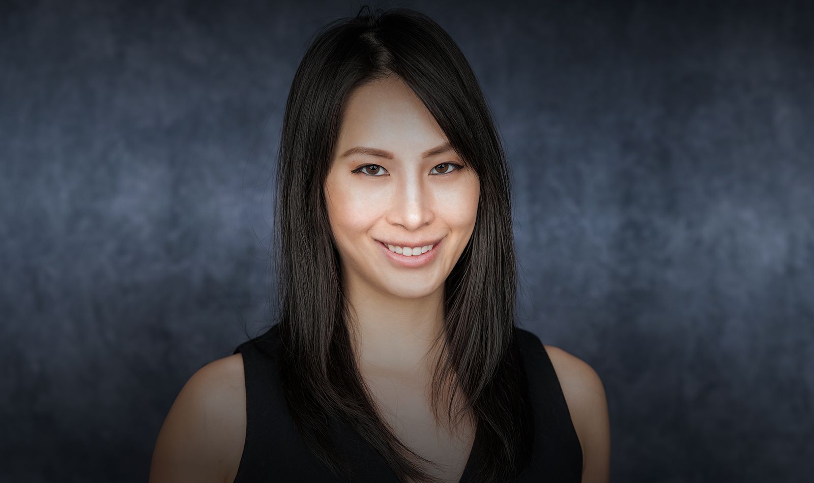 Smiling woman with long black hair, dark background.