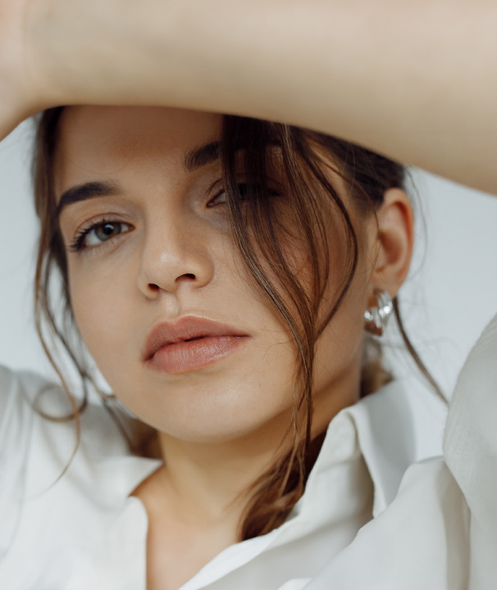 Close-up of a woman with natural makeup wearing earrings and a white shirt