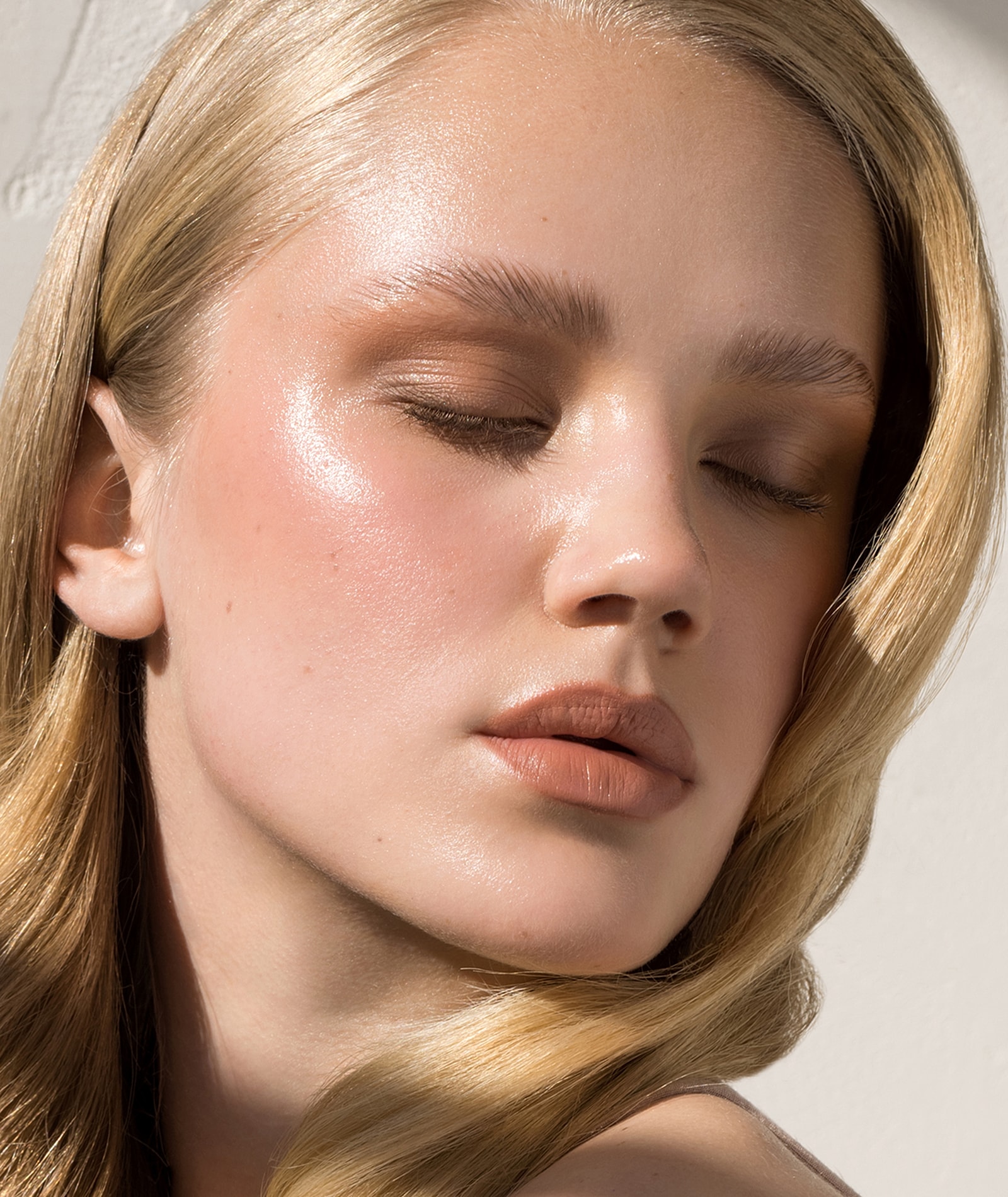 Close-up of model with glowing skin with blonde hair and her eyes closed.